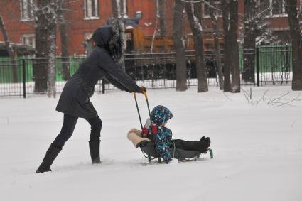 Последствия метели в Москве. Женщина везет ребенка на санках.