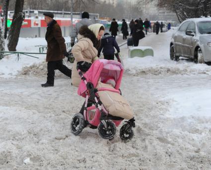 Москва. Девушка везет детскую коляску по неубранной дороге.