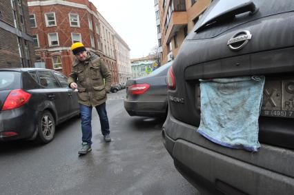 Москва. Корреспондент КП Олег Адамович рядом с припаркованным автомобилем с тряпкой, закрывающей номерной знак.