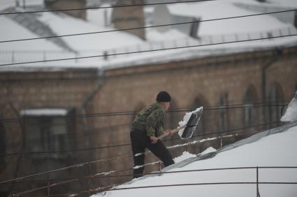Москва. Сотрудник коммунальной службы счищает снег с крыши дома.