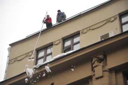 Москва.  Сотрудники коммунальной службы счищают снег с крыши дома.