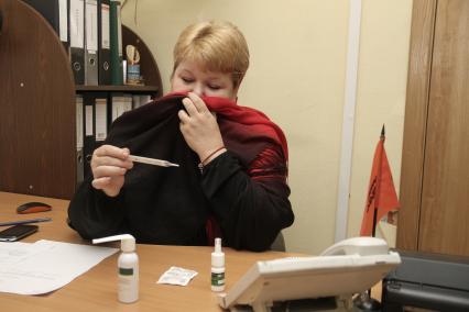 Нижний Новгород. Женщина на рабочем месте в офисе измеряет температуру.