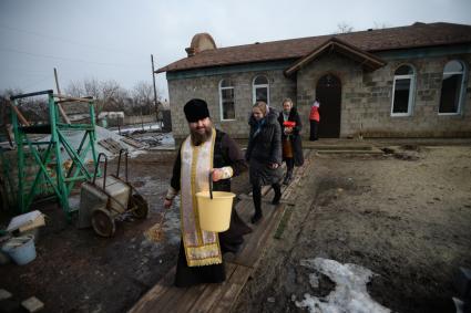 Украина. с.Александровка, Донецкая область. Отец Владимир окропляет святой водой людей рядом с церковью, стоящей на линии фронта.