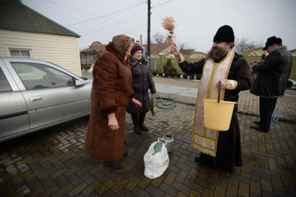 Украина. с.Александровка, Донецкая область. Отец Владимир окропляет святой водой женщин рядом с церковью, стоящей на линии фронта.