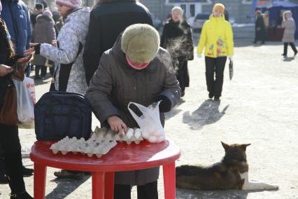 Барнаул. Социальная ярмарка. Женщина перекладывает яйца в пакет.