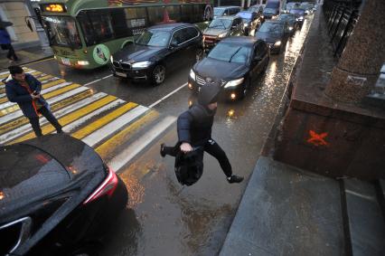 Москва.  Мужчина прыгает через лужу на пешеходном переходе  на Гоголевском бульваре.