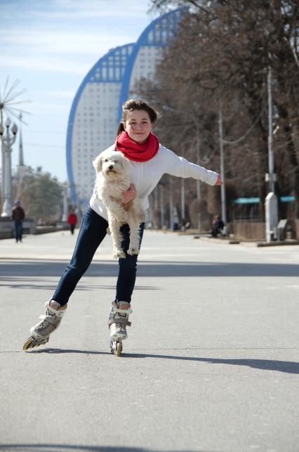 Волгоград. Девушка катается на роликах с собакой на руках.