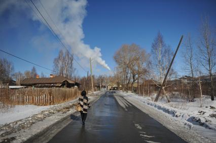 Карабаш. Местная жительница идет по улице на фоне дымящей трубы.