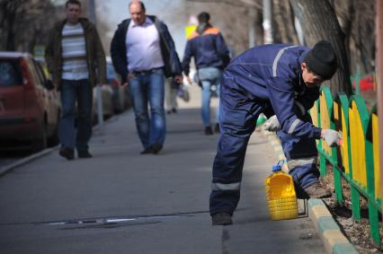 Москва.  Сотрудник коммунальной службы красит  забор.