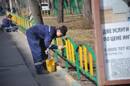 Москва.  Сотрудник коммунальной службы красит  забор.