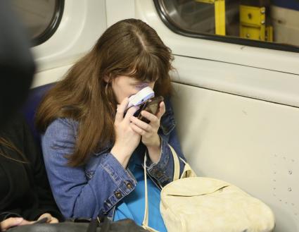 Санкт-Петербург. Девушка смотрит на мобильный телефон через лупу в метро.