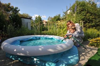 Москва.   Женщина и ребенок  наполняют водой надувной бассейн на дачном участке .