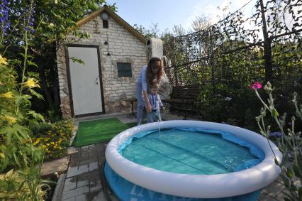 Москва.   Женщина и ребенок  наполняют водой надувной бассейн на дачном участке .