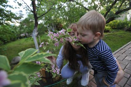 Москва.   Женщина с мальчиком  нюхают цветы  на дачном участке .