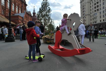 Москва.   Девочка качается на деревянной лошадке  на  историко-гастрономическом  фестивале `Наш продукт` в рамках уличных праздников `Московские сезоны` на Площади Революции.