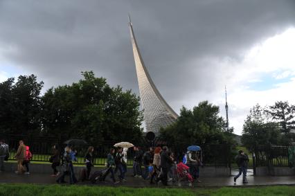 Москва.  Прохожие под дождем в районе станции метро ВДНХ около монумента `Покорителям космоса`.