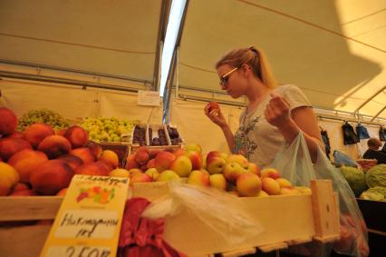 Москва.  Девушка выбирает персики на ярмарке выходного дня.