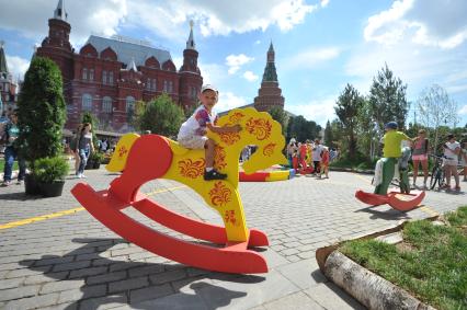 Москва.   Мальчик качается на деревянной лошадке на Манежной площади, где проходит фестиваль `Московское мороженое`.