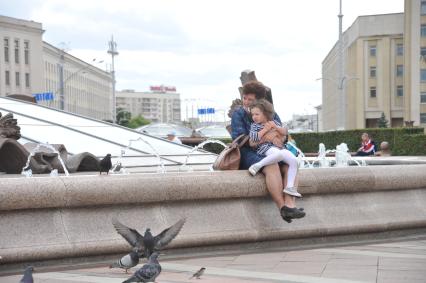 Белоруссия.  Минск. Женщина с девочкой сидит на бортике   фонтана  `Аисты` на площади  Независимости .