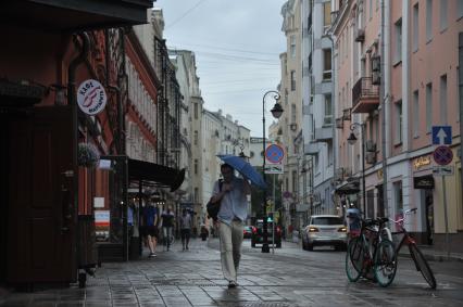 Москва.  Молодой человек под зонтом  идет по  улице Малая Бронная.