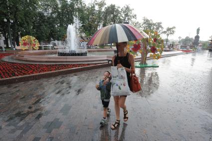 Москва. Женщина с ребенком идет под дождем по Пушкинскому скверу.