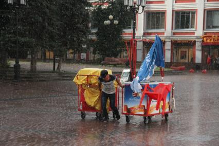 Нижний Новгород.   Мужчина катит  тележки под проливным дождем.