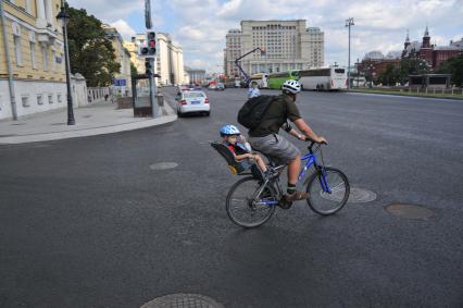 Москва.  Мужчина везет ребенка на велосипеде по Моховой улице.