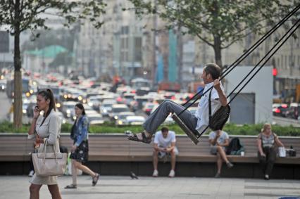 Москва.  Мужчина качается на качелях на Триумфальной площади.