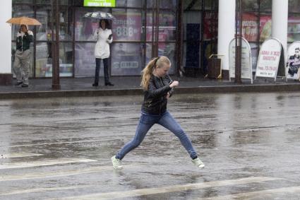 Иркутск. Девушка  перебегает дорогу во время сильного дождя.