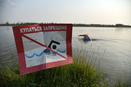 Новосибирск. Мужчина купается в озере возле знака `Купаться запрещено`.