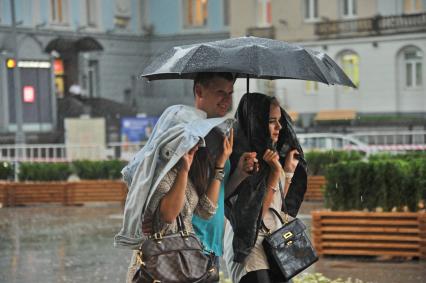 Москва. Молодые люди идут под одним зонтом во время дождя  на Новом Арбате.