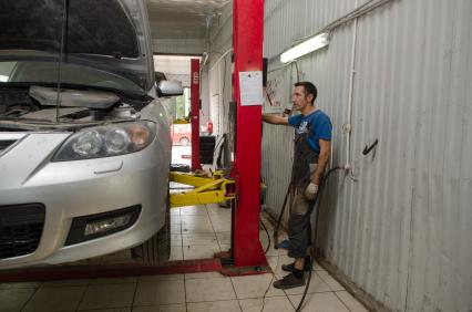 Самара.  Сотрудник автосервиса поднимает автомобиль на подъемнике.