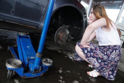 Екатеринбург. Девушка сидит у автомобиля в шиномонтажной мастерской во время замены колеса