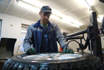 Екатеринбург. Сотрудник шиномонтажной мастерской бортует автомобильное колесо.
