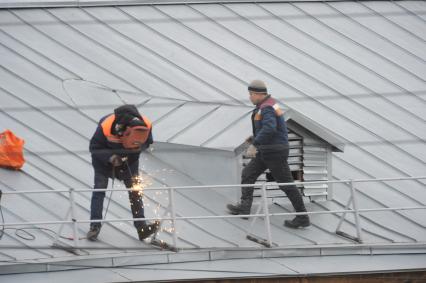 Москва.   Рабочий сваривает ограждение на крыше дома.