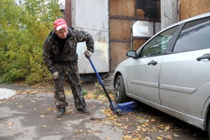Нижний Новгород.  Работник шиномонтажной мастерской поднимает домкратом машину для замены колес.