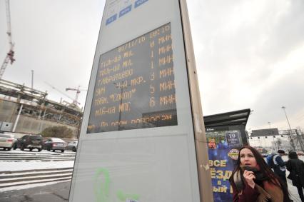Москва. Девушка изучает расписание движения автобусов на остановке.