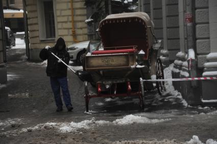 Москва.    Дворник убирает снег с колес старинной кареты на Мясницкой улице.