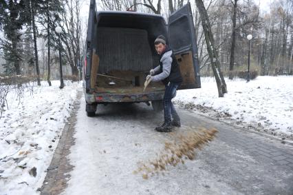 Москва. Дворник посыпает дорожки песком.