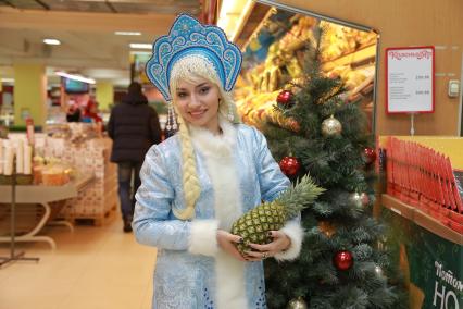 Красноярск. Девушка в костюме Снегурочки выбирает  ананас  в супермаркете.