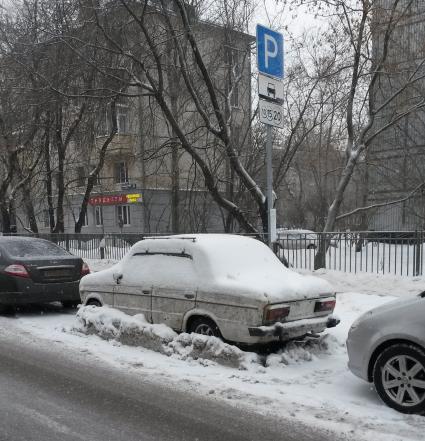 Москва.  Заснеженная машина без номеров на платной парковке.