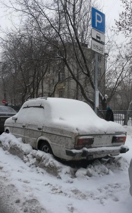 Москва.  Заснеженная машина без номеров на платной парковке.