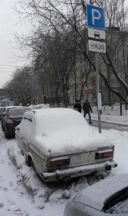 Москва.  Заснеженная машина без номеров на платной парковке.