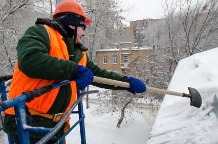 Самара. Сотрудник коммунальной службы счищает снег с крыши дома.