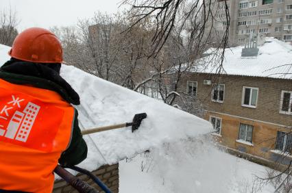 Самара. Сотрудник коммунальной службы счищает снег с крыши дома.