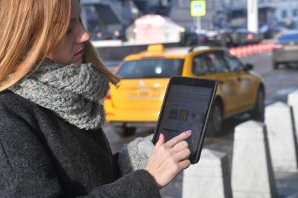 Москва. Девушка вызывает такси при помощи приложения, установленного в планшете.