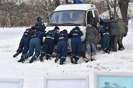 Москва.   Сотрудники МЧС толкают машину