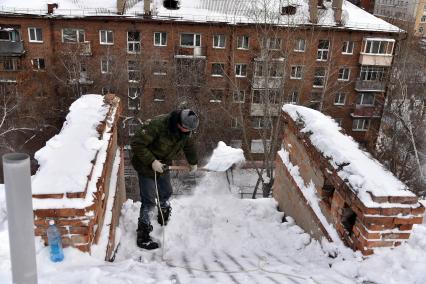 Новосибирск. Дворник на крыше лопатой счищает снег.