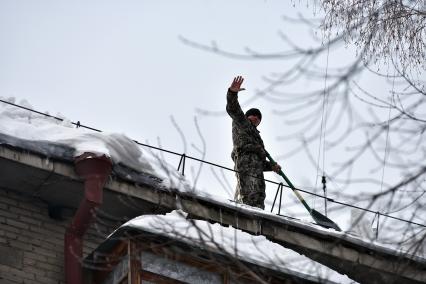 Новосибирск. Дворник  на крыше лопатой счищает снег.