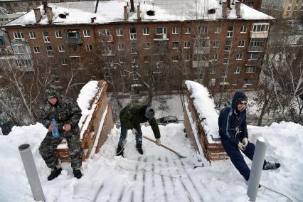 Новосибирск. Дворник на крыше лопатой счищает снег.